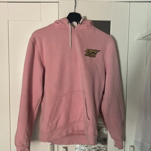 Skate hoodie slime ballz - Rosa hoodie från santa cruiz med fet grafik på ryggen, ärmarna och bröstet. Har huva med snörning och stor magficka. Trycken är i gult, blått och rött och ger en riktigt streetig vibe. Perfekt för dig som gillar skate eller vill sticka ut.