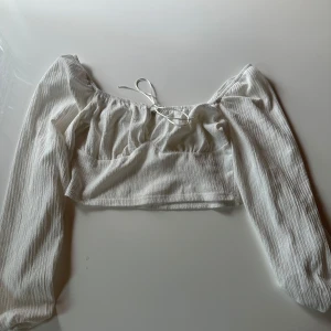 Vit croppad blus från Only Trend - Supersöt vit croppad blus från Only Trend med långa ärmar och offshoulder-modell. Toppen har en lätt rynkad struktur och knytband framtill för extra detalj. Perfekt för dig som gillar en romantisk och trendig look.