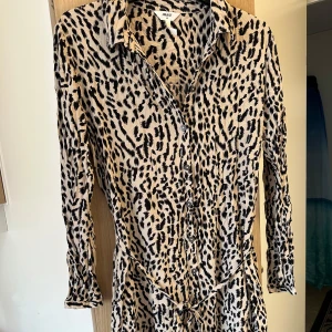 Leopardmönstrad långärmad klänning Object strl: 42 - Säljer en beige och svart leopardmönstrad klänning från Object i storlek 42. Klänningen har lång ärm, knappar framtill och ett knytband i midjan för extra snygg passform. Perfekt för dig som vill sticka ut med ett djuriskt mönster.