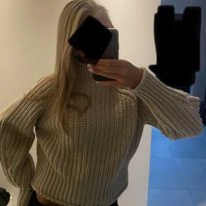 Beige stickad polotröja - Säljer en beige stickad polotröja med grov ribbad struktur och hög hals. Tröjan har långärmade, lite loose ärmar och en mysig passform som ger en chill vibe. Prislappen sitter kvar på tröjan. Perfekt att slänga på sig när det är kallt ute.