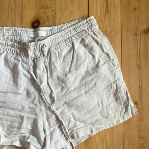 Beige linneshorts från H&M L.O.G.G - Snygga beige shorts från H&M L.O.G.G i storlek 36. De är gjorda i mjukt linne och har en relaxed passform med elastisk midja och snörning. Perfekta för varma dagar och chill stunder. Fickor på sidorna för extra casual vibe. Använda fåtal gånger. Lite skrövliga men som nya efter en strykning❤️😍