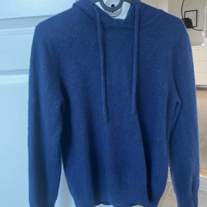 Mörkblå Kashmir  hoodie med huva - Säljer en mörkblå kashmir hoodie med huva och snörning. Tröjan har långärmade ärmar och är gjord i ett mjukt stickat material som känns riktigt skönt mot huden. Den har blivit mindre i tvätten så passar S och mindre