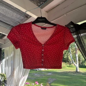 Röd croppad topp med hjärtan från Shein - Supergullig röd croppad topp från Shein med små vita hjärtan över hela. Toppen har v-ringning, korta ärmar och knappar framtill. Ribbad känsla i materialet och perfekt för en söt och trendig look.