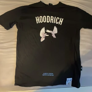 Svart Hoodrich t-shirt med duvor - Svart t-shirt från Hoodrich med tryck av vita duvor både fram och bak. Framsidan har stor HOODRICH-text och motiv, medan baksidan har texten 'From Nothing To Something' i blått och fler duvor. T-shirten har korta ärmar och är gjord i mjuk bomull.