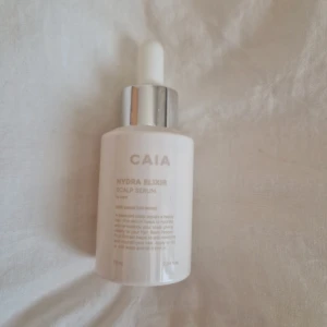 CAIA Hydra Elixir Scalp Serum - Hydra Elixir Scalp Serum från CAIA i en stilren, ljusrosa flaska med silvrig pipett. Innehåller 75 ml och är framtagen för att återfukta och balansera hårbotten. Perfekt för dig som vill ge extra fukt och näring till håret.