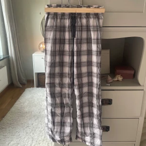 Rutiga bomullsbyxor från H&M - Säljer ett par rutiga byxor från H&M i svart, grått och vitt. Byxorna har resår i midjan med snörning och är tillverkade i 100% bomull. Perfekta för en avslappnad och chill stil.