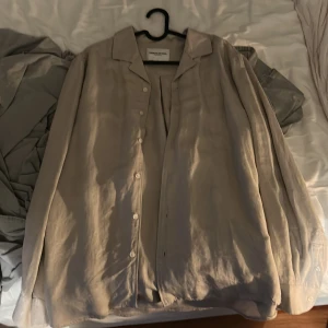 Beige linneskjorta These Glory Days S - Snygg beige skjorta från These Glory Days i storlek S. Skjortan är tillverkad i linne, har klassisk krage, knäppning framtill och långa ärmar. Perfekt för en clean och avslappnad stil.