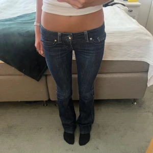 Mörkblå lågmidjade bootcut jeans - Säljer ett par mörkblå jeans med låg midja och bootcut passform från märket guess. Jeansen har snygga detaljer med broderade bakfickor och kontrastsömmar. Om ni vill ha fler bilder eller har frågor om mått är det bara att skriva🩷🩷