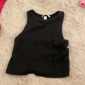 Svart ribbad linnetopp från H&M - En svart ribbad linnetopp från H&M i storlek S. Toppen är croppad och ärmlös med klassisk rund halsringning. Perfekt till jeans eller kjol för en enkel och stilren look. 💗