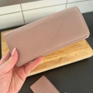 Rosa plånbok med dragkedja - Snygg rosa plånbok med flera fack för kort, mynt och sedlar. Plånboken har en praktisk dragkedja på sidan och tryckknappsstängning. Insidan har transparent ID-fönster och gott om plats för allt du behöver ha med dig💗