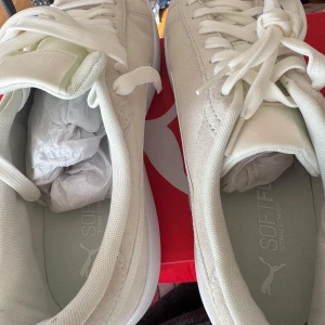Vita sneakers från Puma Softfoam  helt ny  - Fräscha vita sneakers från Puma med Softfoam+ innersula för extra komfort. Skorna har klassisk snörning, rund tå och en stilren design med Pumas logga på sidan och sulan. Ovandelen är i mocka och textil, vilket ger en snygg och modern look. 