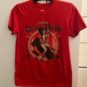 Röd Five Finger Death Punch t-shirt - Snygg röd t-shirt från Five Finger Death Punch med stor tryckt grafik framtill som visar en pinup-tjej på en bomb och coola stjärnor runtom. 