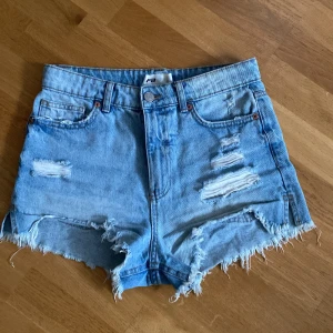 Blå jeansshorts från FB Sister - Snygga ljusblå jeansshorts från FB Sister med hög midja, fransiga kanter. Shortsen har slitna detaljer och klassiska fickor både fram och bak. Du står för frakten, vid mer info skriv