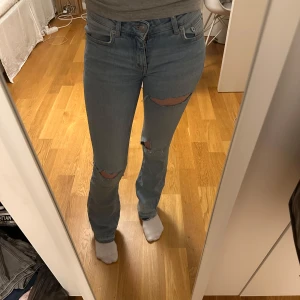 Blå slitna bootcut jeans - Säljer ett par ljusblå jeans med bootcut-modell, har även tre egengjorda hål på knäna och ett lite högre upp. Har även spretat upp dom nere vid fötterna så att dom är lite längre💕