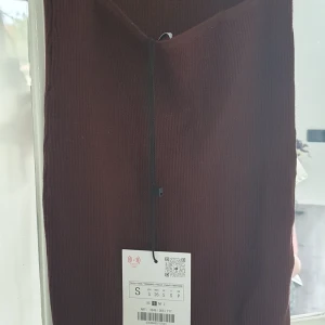 Mörkbrun ribbad långklänning med öppen rygg - Säljer en mörkbrun, ribbad långklänning med tight passform. Klänningen har en snygg öppen rygg med banddetaljer och är ärmlös. Perfekt för dig som vill sticka ut med en stilren och trendig look.