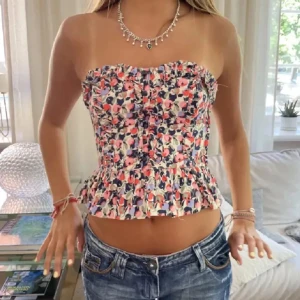 Blommig tubtop!!💖🌸 - Supersöt blommig blus med volangkant nertill och croppad passform. Toppen är ärmlös och har ett färgglatt mönster i rosa, blått, vitt och rött. Perfekt för varma dagar och ger en riktigt somrig vibe.