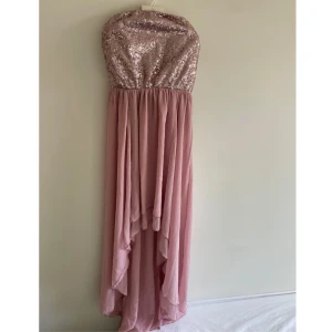 Rosa paljettklänning från Lili - Säljer en superfin långklänning i dusty pink från Lili. Överdelen är axelbandslös och täckt med glittriga paljetter, medan kjolen är i mjukt, flygigt tyg med snyggt fall. Perfekt för dig som vill sticka ut med en glamorös look!  Oanvänd med lapp kvar. Passar bra på bröllop eller när man vill känna sig extra fin. UK 10, motsvarar 38 eller M i storlek.