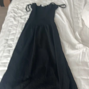 Svart långklänning från H&M - Svart långklänning från H&M med smockad överdel och tunna axelband som kan spännas åt. Klänningen har en flowy kjol. Perfekt för dig som gillar enkel men snygg stil. Aldrig använd, minns tyvärr inte nypris heller 💞