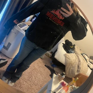 Svart Eminem hoodie med brodyr - Svart hoodie från Eminem The Collection med röd och gul broderad logga på bröstet och ärmen. Klassisk känguruficka, huva med snörning och mjukt material. Perfekt för dig som gillar streetwear och vill sticka ut med en unik merchtröja. Vintage 2000 merch. 