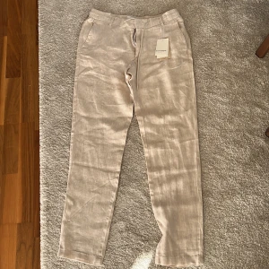 Sandfärgade linnebyxor från Bruun & Stengrade - Snygga sandfärgade linnebyxor från Bruuns Bazaar med dragsko i midjan och raka ben. Byxorna har både sidofickor och bakfickor, perfekt för en chill och stilren look. Luftigt material som passar grymt när det är varmt ute.