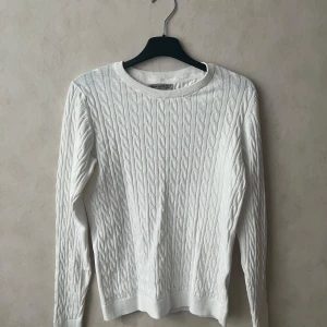 Vit stickad tröja  - Vit kabelstickad tröja från Ullared. Klassisk rund halsringning och långärmad modell. Perfekt för lager-på-lager och enkel att matcha med jeans eller kjol. En pytteliten smink fläck som garanterat går bort i tvätt.