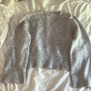 Grå stickad tröja från Gina Tricot - Mysig grå stickad tröja från Gina Tricot med v-ringad hals och breda ribbade muddar vid ärmslut och nederkant. Perfekt för kyliga dagar och enkel att matcha med jeans eller kjol. Mjuk och skön känsla, passar dig som gillar klassisk stil. Den är realativt overzized. Så jag som vanligtvis har S kunde ha denna och satt perfekt .