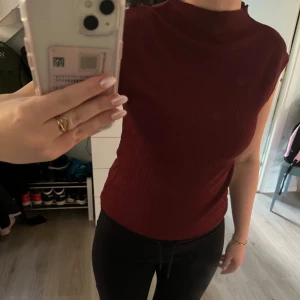 Vinröd strukturerad topp - Säljer en vinröd topp med struktur och hög hals. Toppen är ärmlös. Storlek S. Aldrig använd.