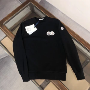Svart sweatshirt från Moncler - Svart sweatshirt från Moncler med klassisk rund hals och broderad logotyp på bröstet och ärmen. Tröjan har en stilren look med ribbade muddar och är perfekt för dig som gillar exklusiva streetwear-vibbar.