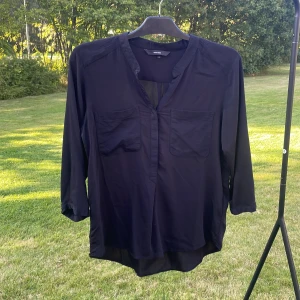 Svart blus från Vero Moda, M - Svart blus från Vero Moda i storlek M. Modellen har två bröstfickor, v-ringad hals och trekvartsärmar. Materialet är lätt och tunt, perfekt för en chill och stilren look. Passformen är normal och blusen har en enkel, tidlös design utan mönster.