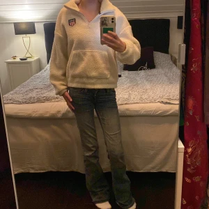 Vit fleece hoodie från GANT - Mysig vit hoodie från GANT i fleece med half zip och stor känguruficka framtill. Tröjan har lång ärm, hög krage och ett broderat GANT-märke på bröstet. Perfekt för kalla dagar när du vill vara både chill och varm.