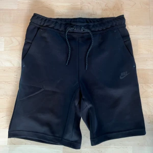 Svarta shorts från Nike - Svarta shorts från Nike med slim fit och avsmalnande ben. De har snörning i midjan, sidofickor och en bakficka med dragkedja. Perfekta för träning eller avslappnade dagar. Materialet känns mjukt och sportigt.