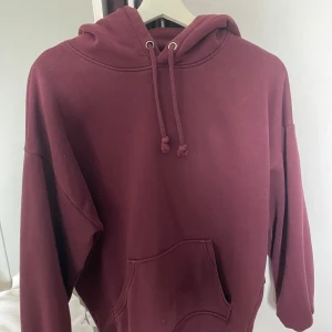 Vinröd hoodie från BikBok - Mysig vinröd hoodie från BikBok med huva och dragsko. Tröjan har en stor magficka och långa ärmar. Perfekt för kyliga dagar när du vill vara både bekväm och snygg.