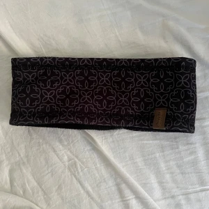 Svart pannband med mönster från Lindberg - Svart pannband från Lindberg med grått blommigt mönster. Utsidan är i mjuk polyester och insidan är fodrad med fleece för extra värme. Perfekt för kyliga dagar och sitter bekvämt runt huvudet.