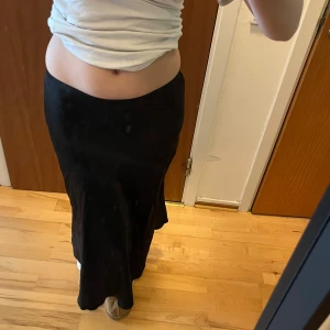 Svart långkjol i satin - Säljer en svart långkjol i glansigt satinmaterial. Kjolen har en smal passform upptill och faller snyggt längs benen. Perfekt att styla med en enkel topp eller stickad tröja. den går upp lite över anklarna så ni är medvetna 💞