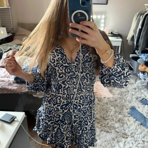 Blåvit mönstrad kortklänning från Zara - Säljer en blåvit kortklänning från Zara med unikt mönster och v-ringning. Klänningen har långa ärmar med lätt puff och knytning vid halsen. Perfekt till skolavslutningen!! köpt för 700
