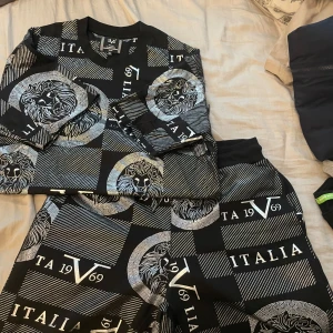 Svarta shorts och t-shirtmed lejonmönster från V1969 Italia - Säljer ett par svarta shorts från V1969 Italia med grafiskt lejonmönster och vita tryck. Shortsen har snörning i midjan och är perfekta för en trendig look. Mjukt material och normal passform.helt ny köpt för 6000 säljer som set 