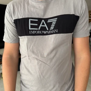 Grå t-shirt från Emporio Armani EA7 - Snygg grå t-shirt från Emporio Armani EA7, skön kvalité som passar till de mesta ! Tyvär ingen storlek men skulle gissa på M 