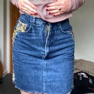 Jeanskjol med blommiga detaljer - Säljer en mörkblå jeanskjol med unika blommiga tygpaneler på sidorna💚💙Köpt second hand och fått många komplimanger när jag använt denna! Säljer för att den tyvärr börjar bli för liten för mig:/ 