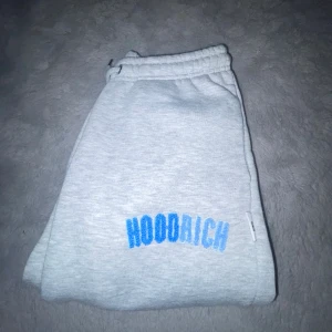 Grå mjukisbyxor från Hoodrich - Grå mjukisbyxor från Hoodrich med blå broderad logga på benet. Byxorna har resår och snörning i midjan för extra komfort. Perfekta för en avslappnad stil och enkel att matcha med olika toppar. Pris går att diskutera!