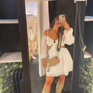 Vit kortklänning med cut-out och ballongärmar - Säljer en söt vit kortklänning med ballongärmar och smala axelband. Klänningen har v-ringning, cut-out vid midjan och omlottdetalj framtill. Perfekt för sommarens alla tillfällen!