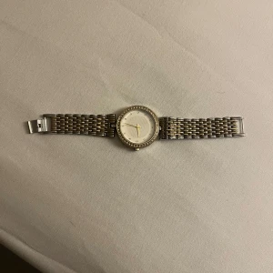 Silver vintage klocka med glittrig urtavla - Säljer en elegant vintage klocka från Swissme med silverfärgat armband i metall och rund urtavla. Urtavlan är vit med glittriga detaljer runt kanten och har en klassisk design. Perfekt accessoar för att lyfta din stil.