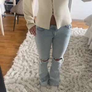 Ljusblå bootcut jeans med hål - Säljer ett par ljusblå jeans med bootcut passform och slitningar vid knäna. Jeansen är lågmidjade. St S/M från MEET ME THERE.