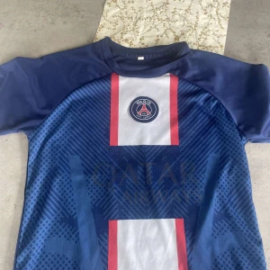 PSG Mbappé matchtröja - Säljer en blå PSG fotbollströja med Mbappé och nummer 7 på ryggen. Tröjan har korta ärmar, vita och röda detaljer framtill samt PSG-logga på bröstet. Materialet är lätt och andas, perfekt för fotbollsträning eller match. Nypris 1299, köpt i Paris.