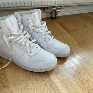 Nike Air Force 1 Mid vita sneakers - Säljer ett par helvita Nike Air Force 1 Mid sneakers med klassisk design. Använd några gånger och har lite smuts men det ska gå att tvätta bort väldigt enkelt 