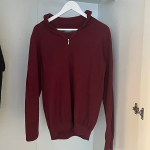 Vinröd tröja med dragkedja - Vinröd långärmad tröja med liten dragkedja vid halsen och ribbade muddar. Perfekt för kyligare dagar och enkel att matcha med olika outfits.