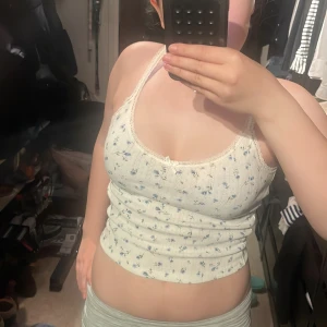 Vit blommig ribbad linnetopp från H&M Divided - Säljer en söt vit ribbad linnetopp från H&M Divided med små blå blommor och spetsdetalj vid halsringningen.