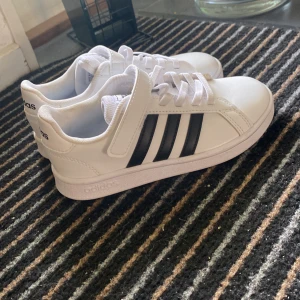 Vita Adidas sneakers med svarta ränder - Säljer ett par fräscha vita Adidas sneakers med klassiska svarta ränder på sidorna. Har använts 1 - 2 gånger men dom är jätte fina, detta skor passar till barn och storlek är 30