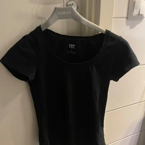 Svart kortärmad topp från 157 - En enkel svart topp från 157 i storlek XS. Modellen har rund halsringning och korta ärmar. Bekväm att ha på sig när som! 
