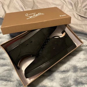 Svarta sneakers från Christian Louboutin - Säljer ett par svarta sneakers från Christian Louboutin med klassisk röd sula. Skorna har snörning och är tillverkade i en kombination av skinn och mocka. Snygg och stilren design med diskreta detaljer, levereras med originalkartong och dustbag.