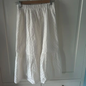 Vit långkjol med broderade detaljer från Lindex - Säljer en vit broderad långkjol från Lindex barnavdelning. Kjolen har en luftig och flowy passform, perfekt för varma dagar. 🌼🫧